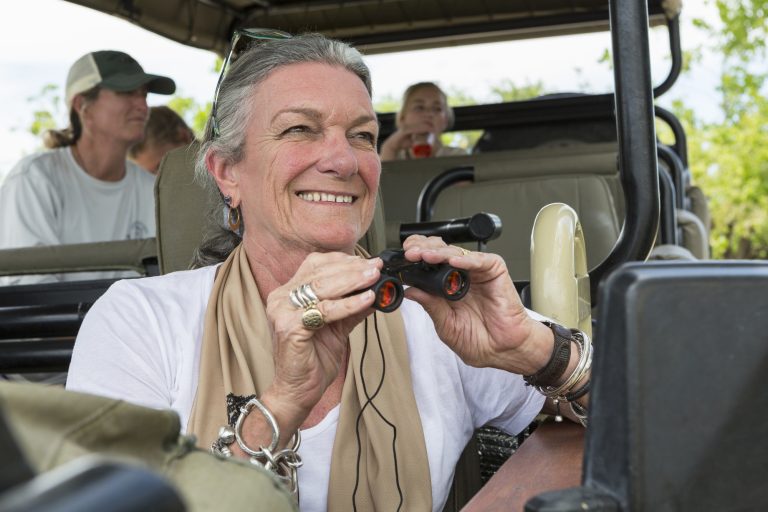 A family in a safari jeep in a wildlife reserve, a seniorwoman with binoculars.