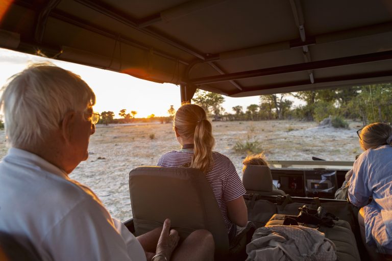Three generations of a family on safari, in a jeep out at sunset.